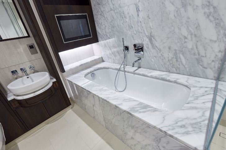 marble bath with dark wood cabinets and television